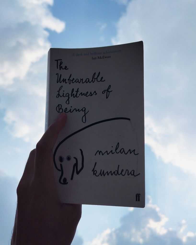 Holding the book The Unbearable Lightness of Being against the background of sky with clouds
